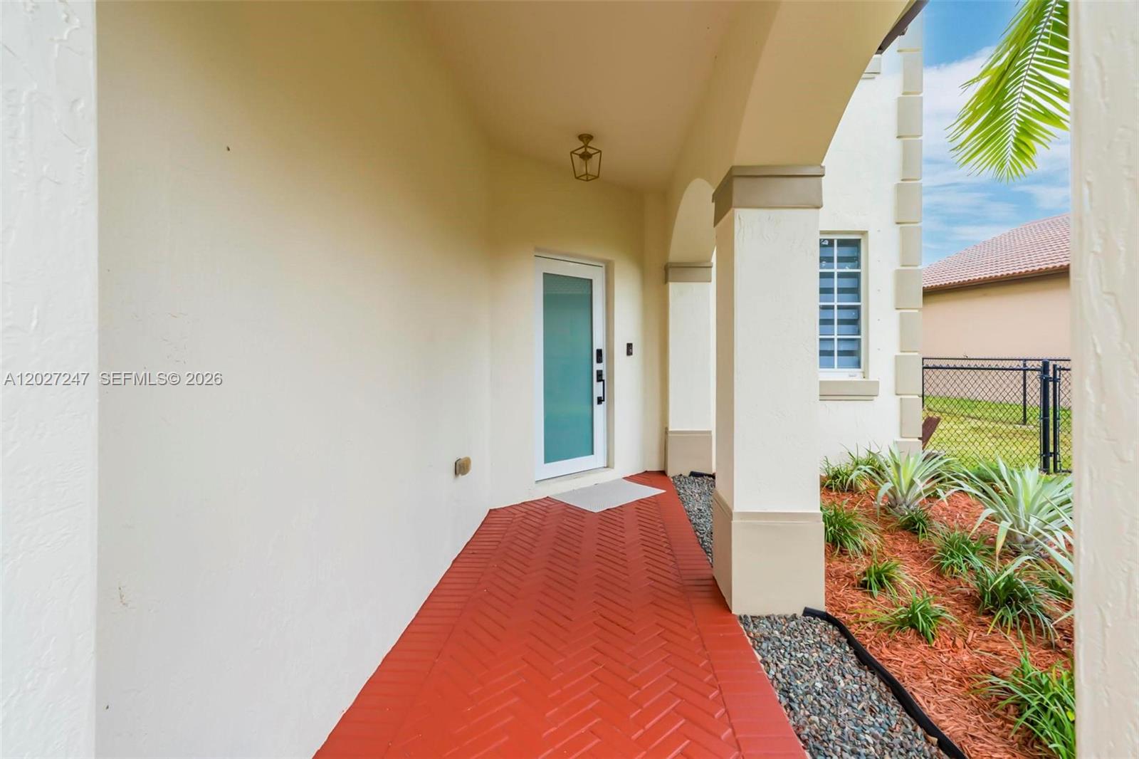 A covered entryway features a red herringbone brick floor and a modern glass front door — 156 SE 22nd Ter, Homestead FL 33033, HOMESTEAD, FL