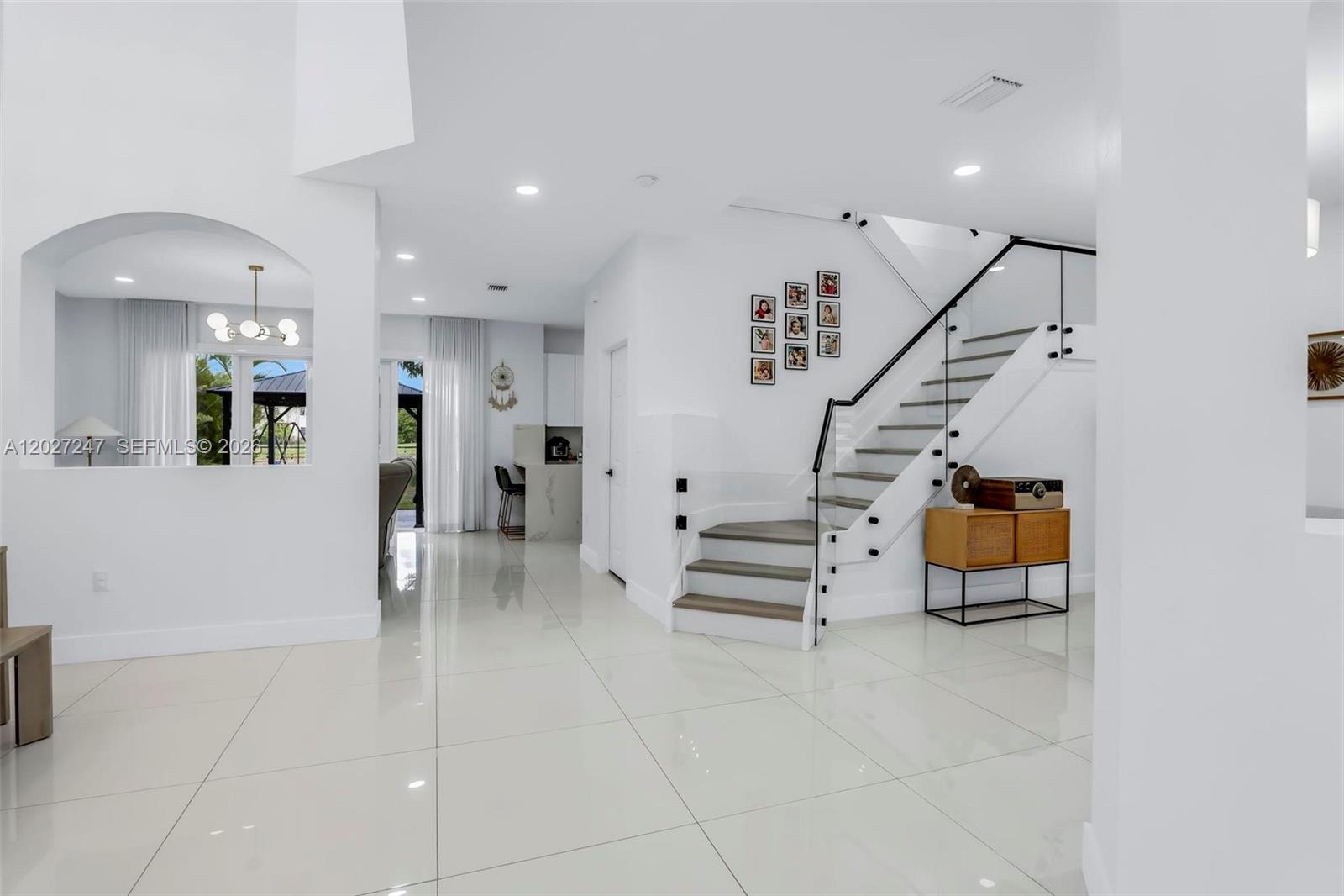 A bright, modern foyer features white tile floors, a staircase with glass railings, and wall art — 156 SE 22nd Ter, Homestead FL 33033, HOMESTEAD, FL