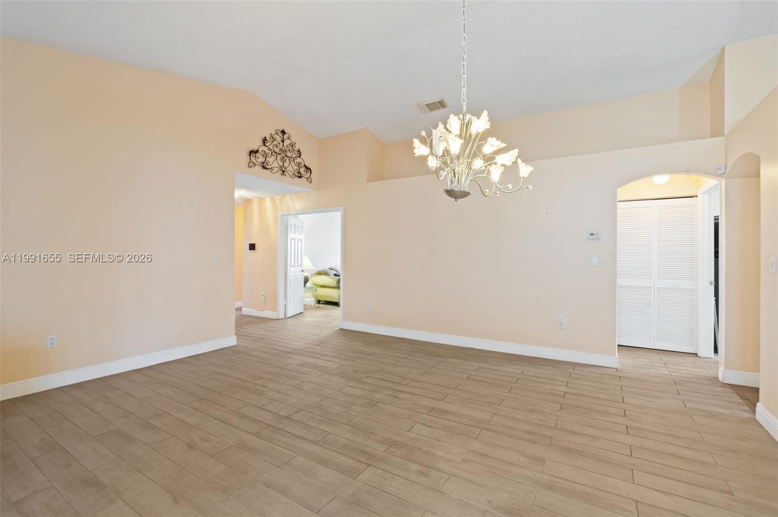 An empty room features light-colored walls, wood-look tile flooring, and a decorative floral chandelier — 12556 NW 10th Pl, Sunrise FL 33323, SUNRISE, FL