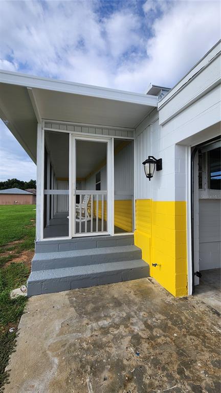 A screened-in porch with gray steps sits beside a white and yellow block wall — 17653 BROAD STREET, MONTVERDE, FL