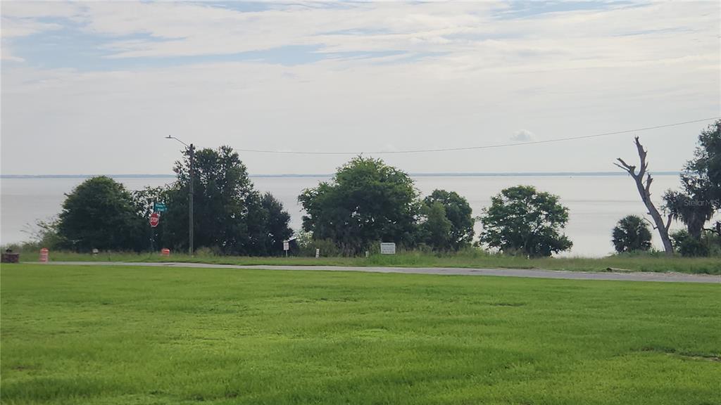 A grassy field overlooks a body of water with trees and a road in the background — 17653 BROAD STREET, MONTVERDE, FL