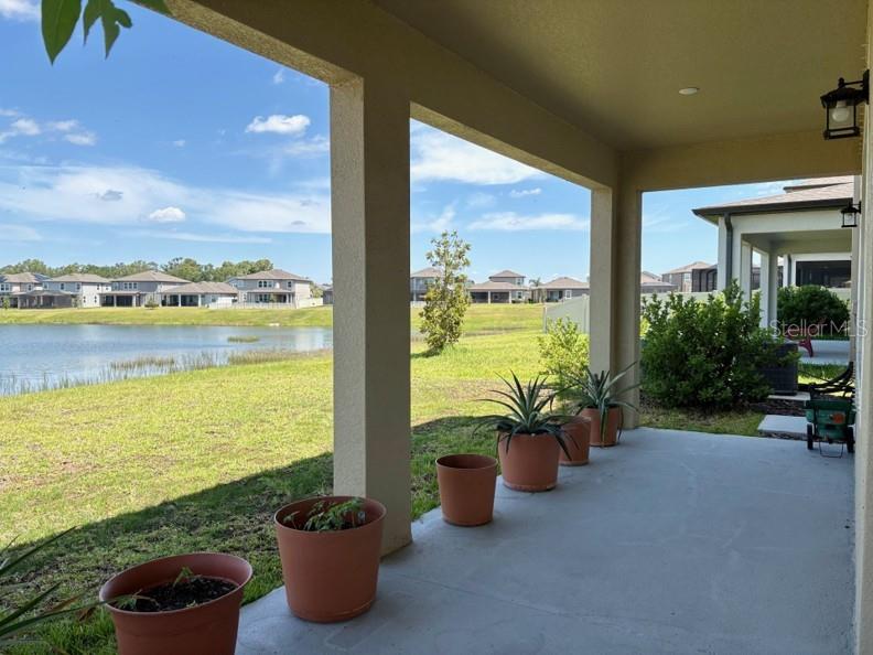 A covered concrete patio overlooks a grassy lawn and a lake with houses beyond — 3091 MARINE GRASS DRIVE, WIMAUMA, FL