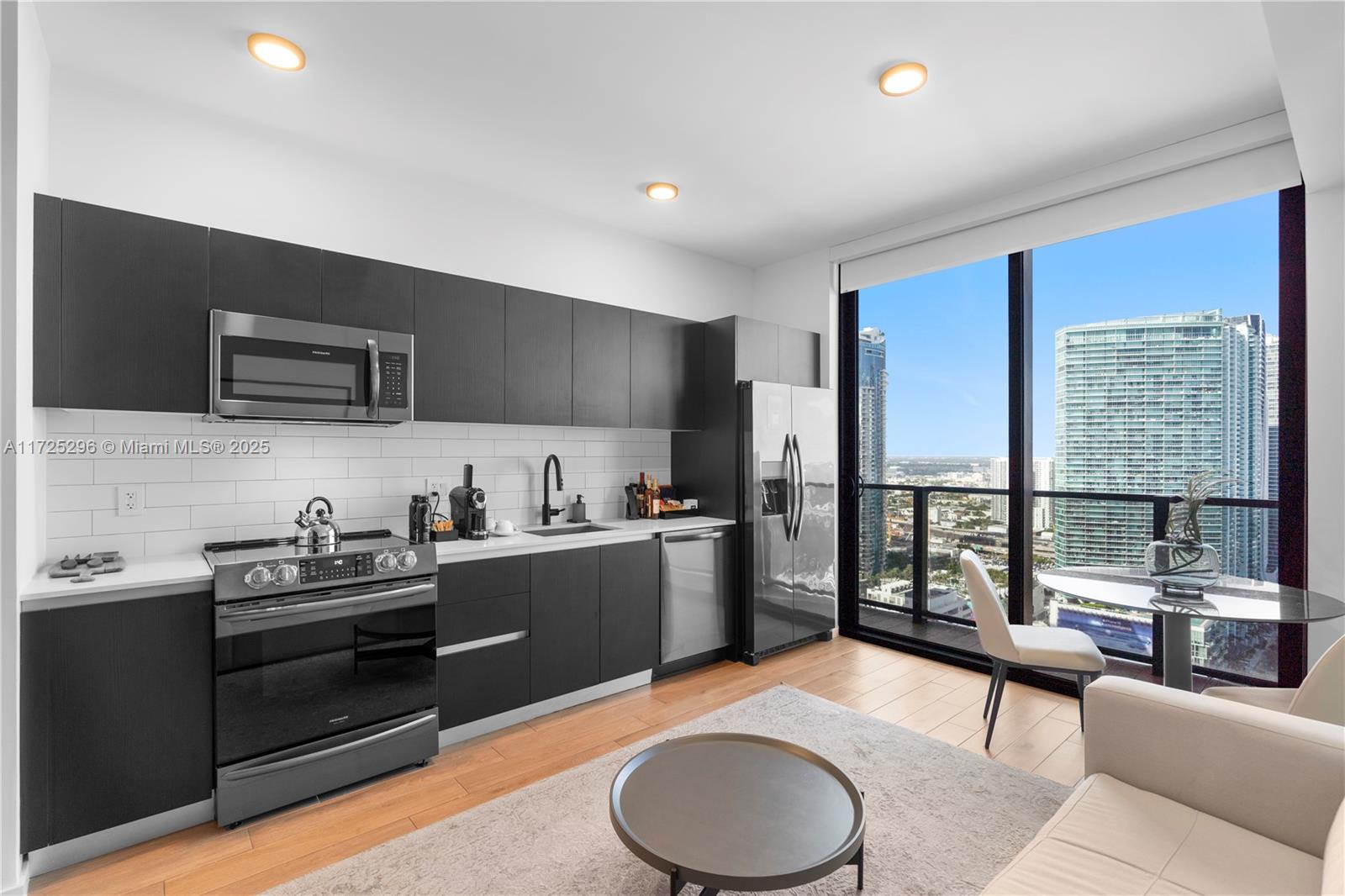 A modern kitchen features dark cabinetry, stainless steel appliances, and a view of city skyscrapers — 398 NE 5th St # 3207, Miami FL 33132, MIAMI, FL