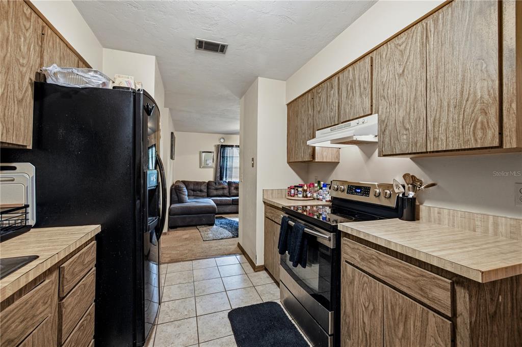 A galley kitchen features wood-grain cabinets, laminate countertops, and a black refrigerator and stove — 2902 NW 39TH PLACE, GAINESVILLE, FL