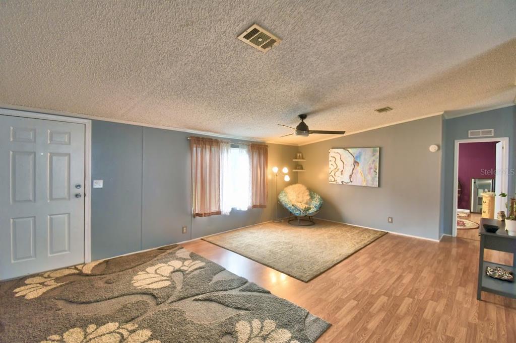 A living room features light blue walls, wood-look flooring, two area rugs, and a ceiling fan — 1750 W FROSTPROOF ROAD, FROSTPROOF, FL