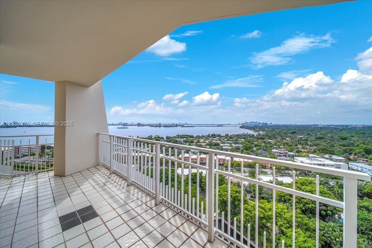 A tiled balcony with a white railing overlooks a bay and surrounding greenery — 1000 Quayside Ter # 10, Miami FL 33138, MIAMI, FL