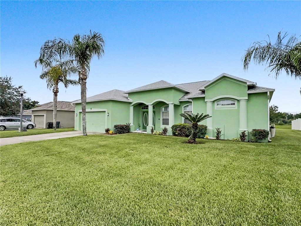 A single-story, light green house with a two-car garage and palm trees in the yard — 8155 WOODVINE CIRCLE, LAKELAND, FL