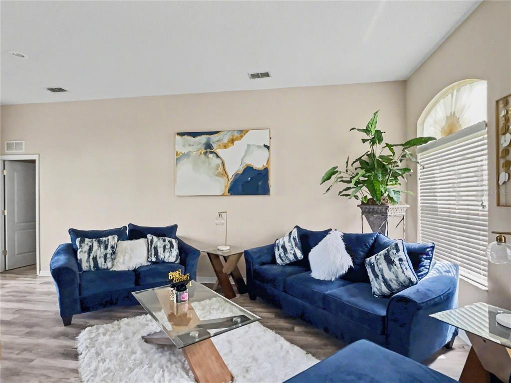 A living room features two blue velvet sofas, a glass coffee table, and abstract wall art — 8155 WOODVINE CIRCLE, LAKELAND, FL