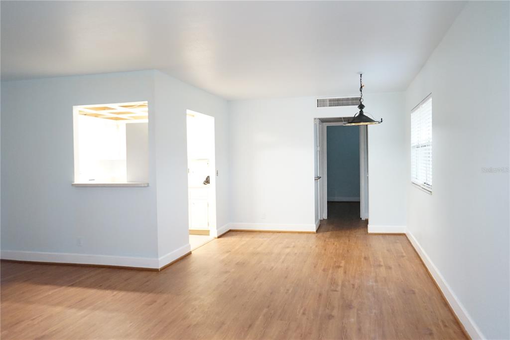 An empty room with light-colored walls, wood-look flooring, a pass-through window, and a hanging light — 201 BEDFORD TRAIL UNIT 138, SUN CITY CENTER, FL