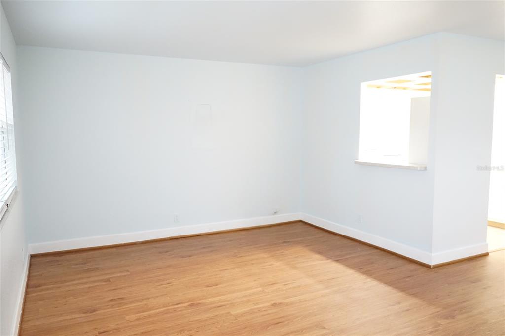 An empty room with light blue walls, wood-look flooring, and a window pass-through — 201 BEDFORD TRAIL UNIT 138, SUN CITY CENTER, FL