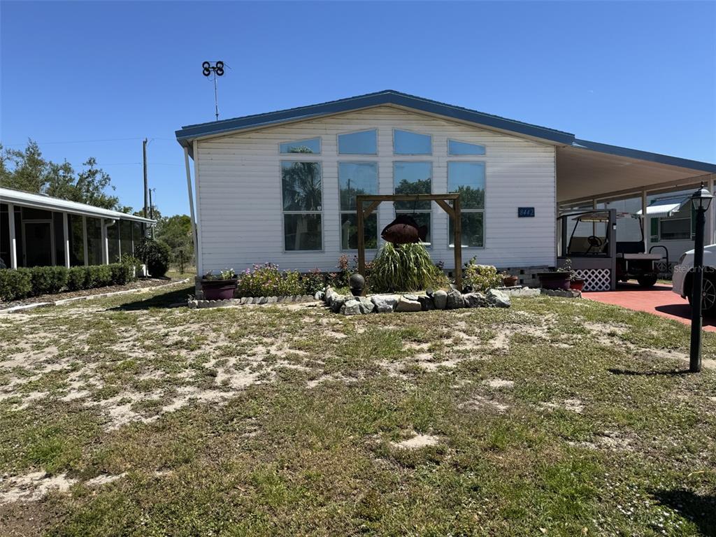 A white manufactured home features a front yard, a carport, and a wooden garden trellis — 8442 BREEZE HILL DRIVE, LAKE WALES, FL