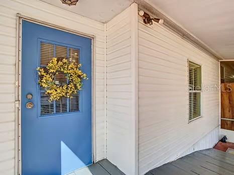 A blue front door with a yellow wreath stands on a porch with white siding — 8442 BREEZE HILL DRIVE, LAKE WALES, FL