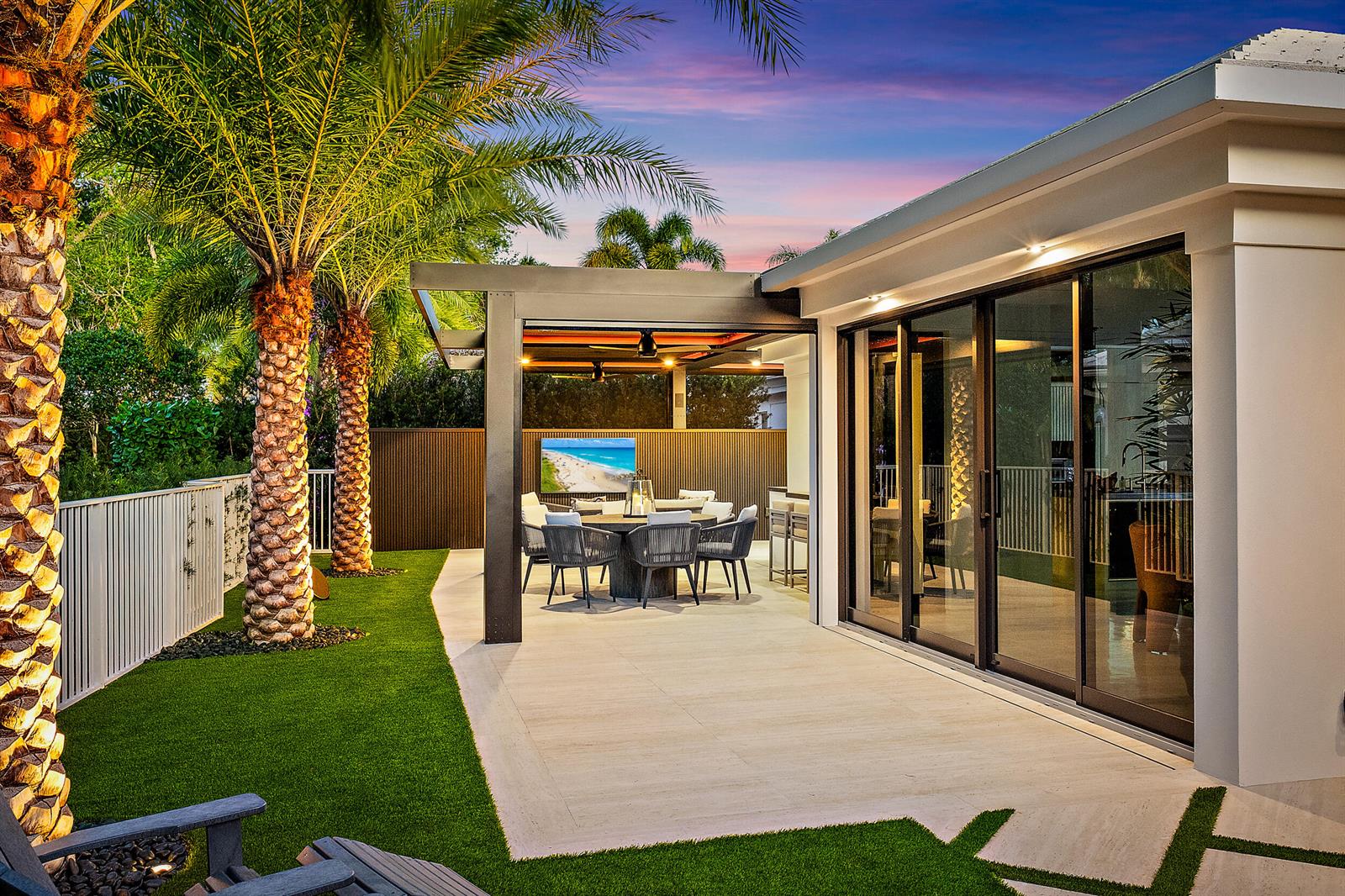 A patio with a pergola, outdoor dining set, and television sits beside a modern house — 3501 Captains Way, Jupiter FL 33477, JUPITER, FL