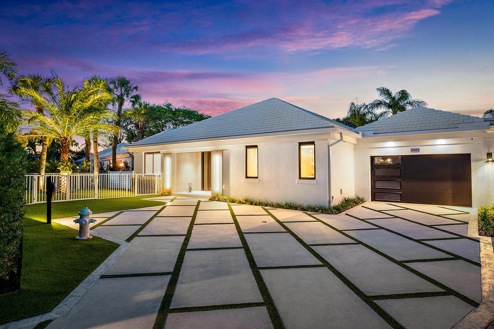 A modern white house with a geometric concrete driveway and a dark garage door at dusk — 3501 Captains Way, Jupiter FL 33477, JUPITER, FL