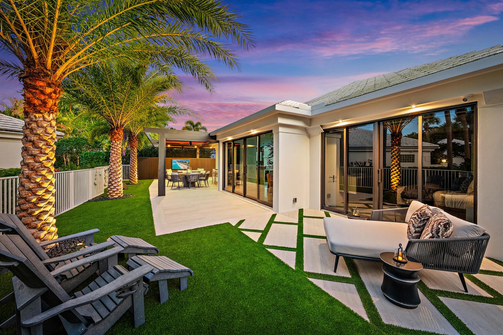 A backyard patio features a lounge chair, dining area, artificial turf, and palm trees at sunset — 3501 Captains Way, Jupiter FL 33477, JUPITER, FL