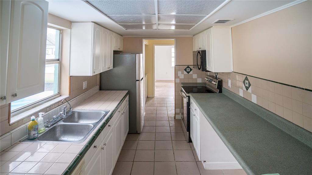 A galley kitchen features white cabinets, tiled countertops, a stainless steel refrigerator, and tile flooring — 3320 LAS BRISAS DRIVE, RIVERVIEW, FL