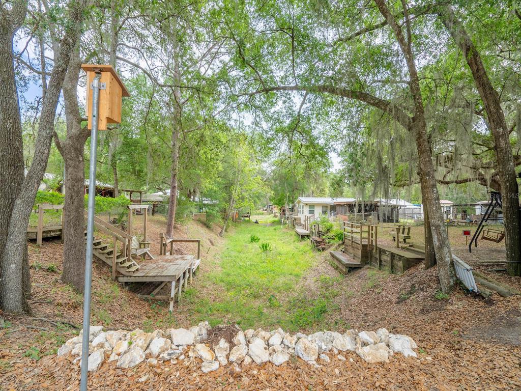 A grassy drainage ditch separates two wooden decks beneath a canopy of large oak trees — 21220 E HIGHWAY 316, FORT MC COY, FL