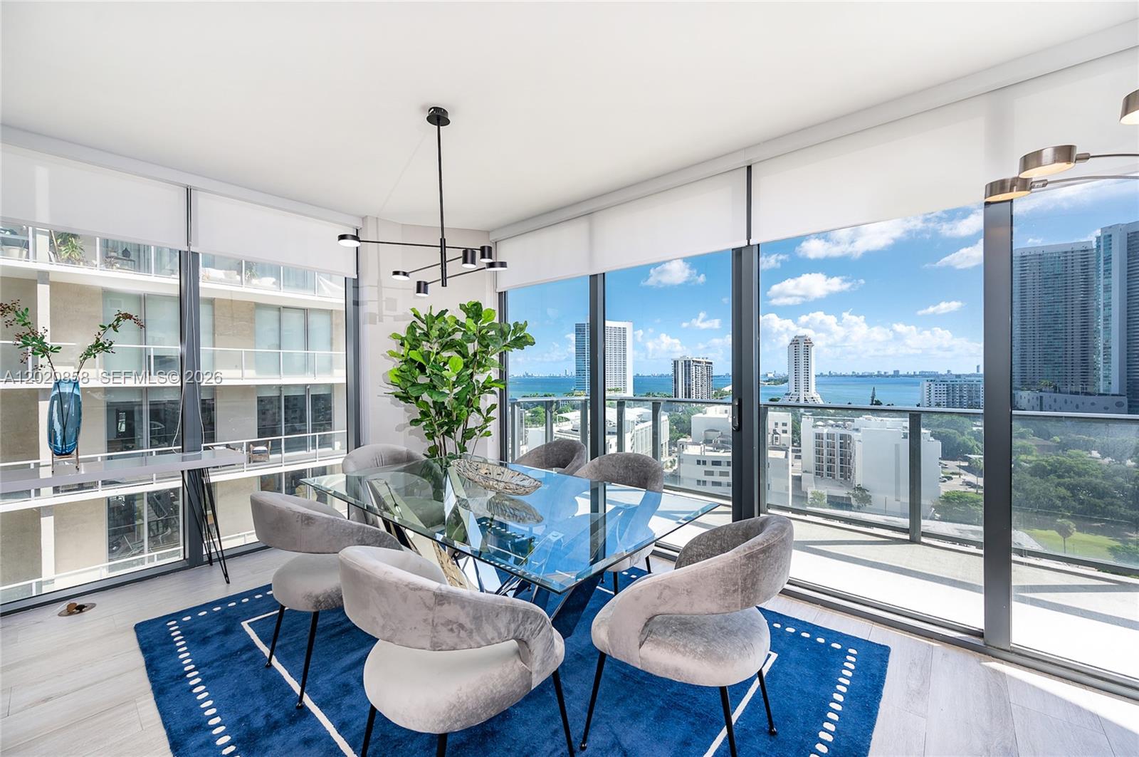 A dining room features a glass table, velvet chairs, and floor-to-ceiling windows overlooking the city — 121 NE 34th St # 1408, Miami FL 33137, MIAMI, FL