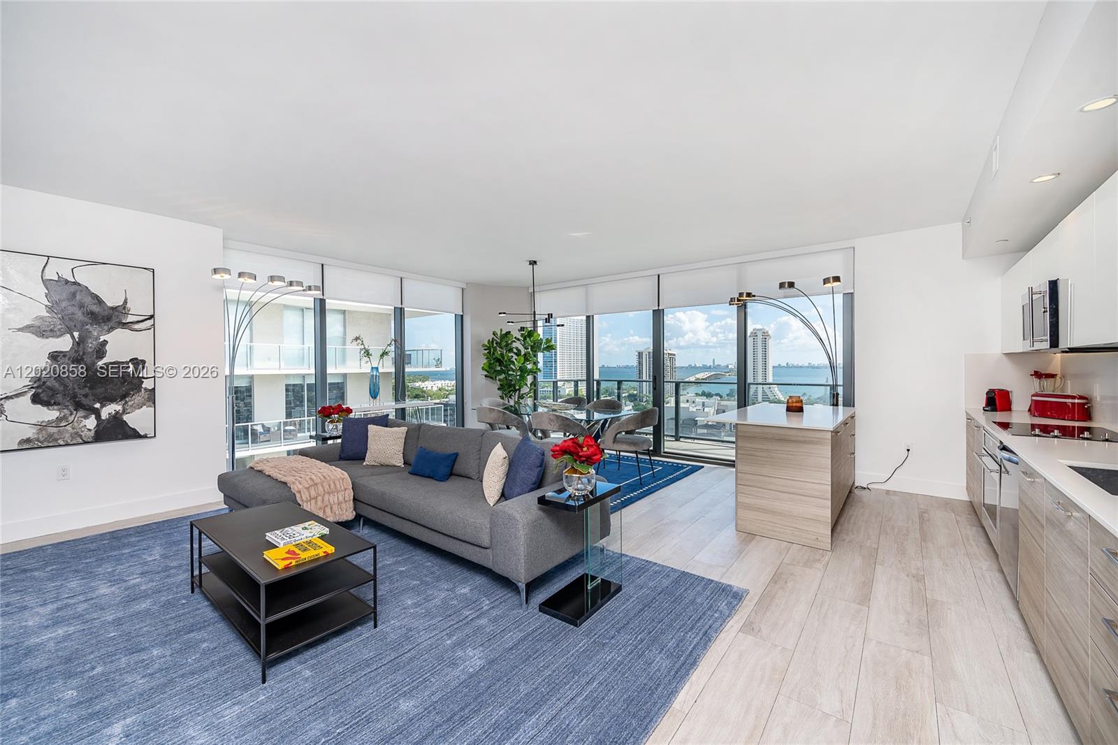 An open-concept living area features a grey sectional, kitchen, and floor-to-ceiling windows with water views — 121 NE 34th St # 1408, Miami FL 33137, MIAMI, FL