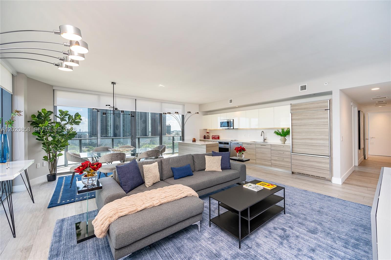 An open-concept living room and kitchen feature a grey sectional, dining area, and city views — 121 NE 34th St # 1408, Miami FL 33137, MIAMI, FL