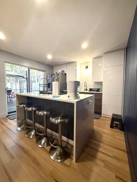 A modern kitchen features a white island with bar stools, light wood flooring, and cabinetry — 22184 Boca Rancho Drive # A, Boca Raton FL 33428, BOCA RATON, FL