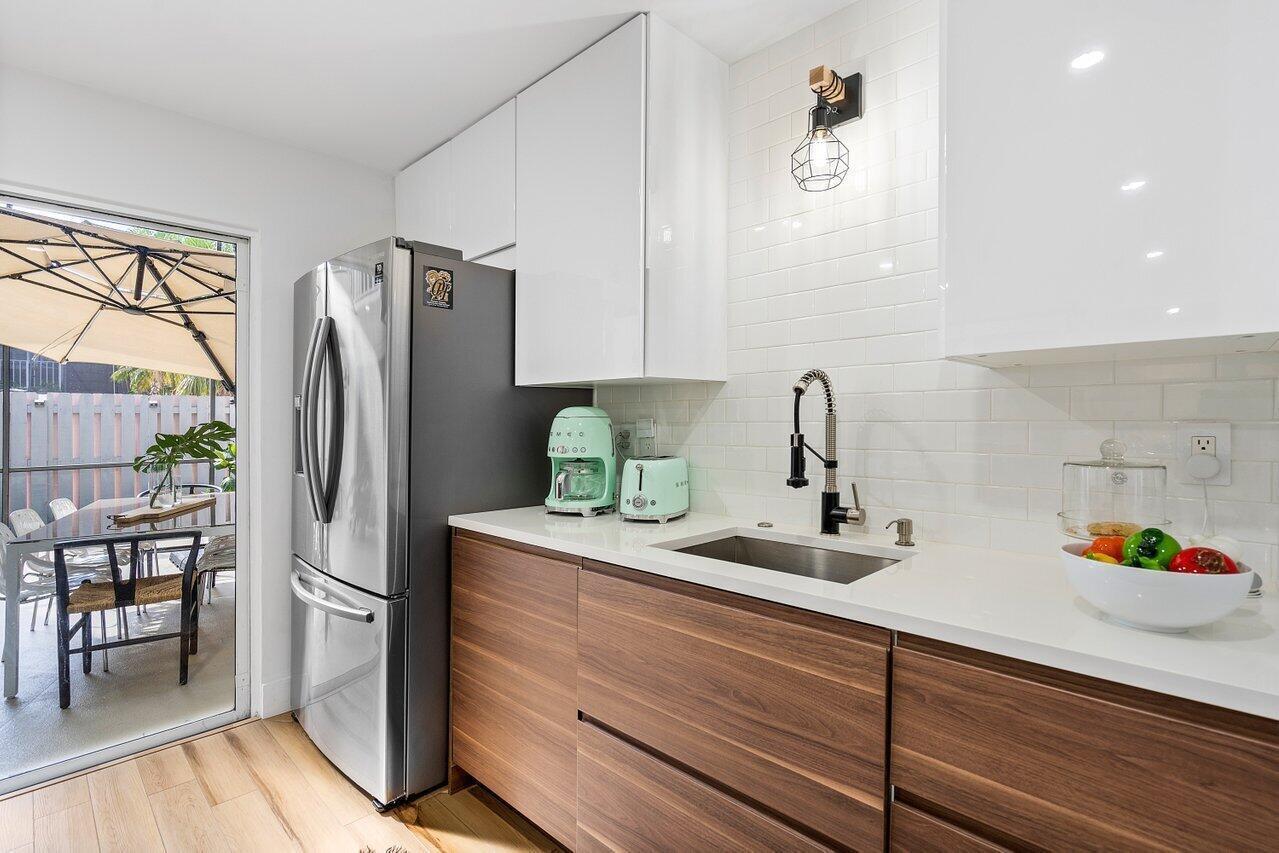 A modern kitchen features wood-grain lower cabinets, white upper cabinets, a stainless refrigerator, and a sink — 22184 Boca Rancho Drive # A, Boca Raton FL 33428, BOCA RATON, FL