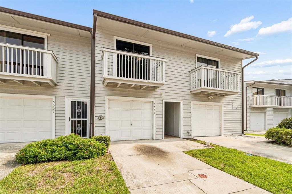 A row of two-story townhouses with light-colored siding, white garage doors, and small upper-level balconies — 6437 93RD TERRACE N UNIT 5002, PINELLAS PARK, FL