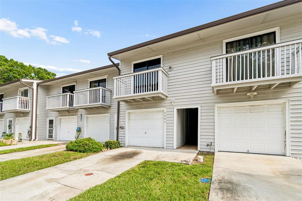 A row of two-story townhomes with light gray siding, white garage doors, and small upper balconies — 6437 93RD TERRACE N UNIT 5002, PINELLAS PARK, FL