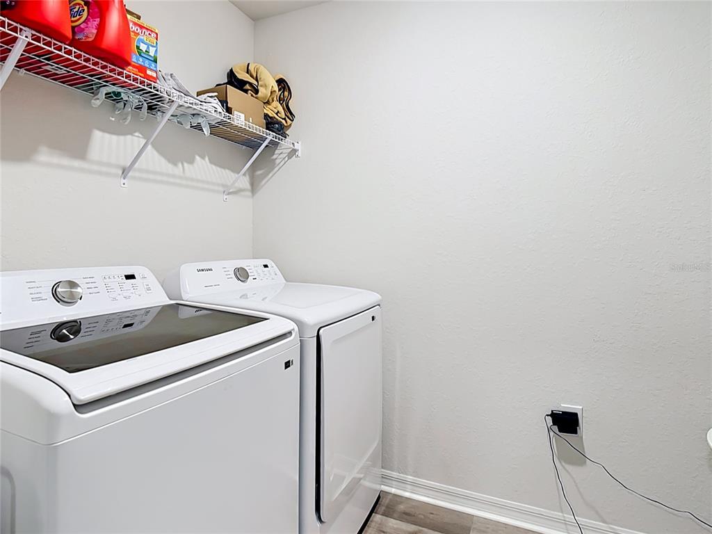 A laundry room features two white Samsung appliances, a wire shelf, and a wall outlet — 371 CROSSINGS AVENUE, ST CLOUD, FL