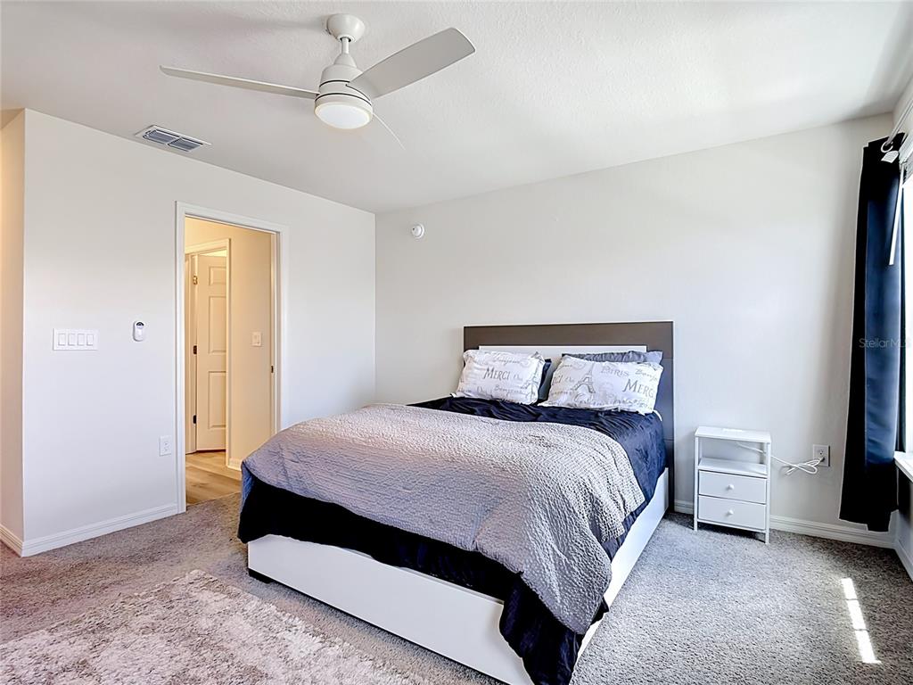 A bedroom features a bed with a grey quilt, a ceiling fan, and a nightstand — 371 CROSSINGS AVENUE, ST CLOUD, FL