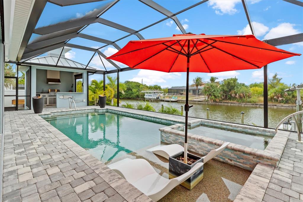 A screened-in pool area features a spa, lounge chairs, an umbrella, and an outdoor kitchen — 15650 MEACHAM CIRCLE, PORT CHARLOTTE, FL