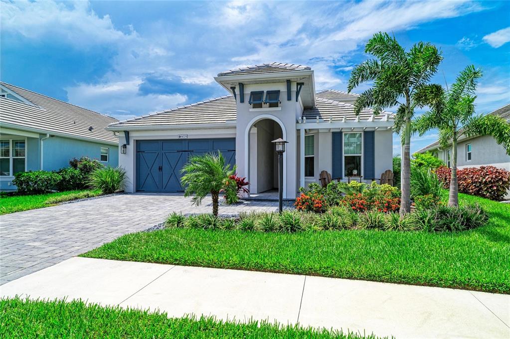 A single-story house with a blue garage door, arched entryway, and landscaped front yard — 8079 SLIPWAY DR, SARASOTA, FL