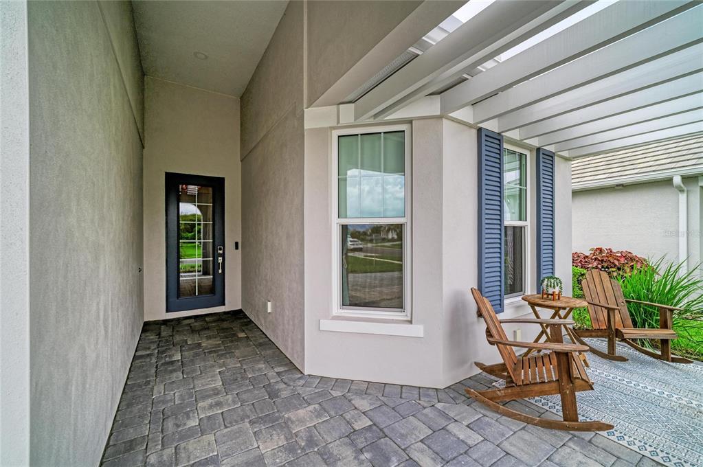 A covered patio features stone pavers, two wooden rocking chairs, and a dark-framed glass door — 8079 SLIPWAY DR, SARASOTA, FL
