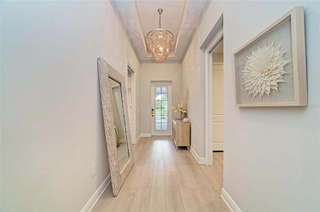 A bright entryway features light wood flooring, a beaded chandelier, a floor mirror, and console — 8079 SLIPWAY DR, SARASOTA, FL