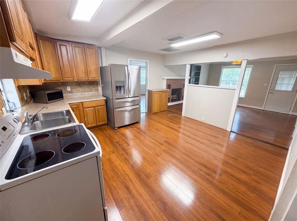 A kitchen with wood cabinets, stainless steel appliances, and hardwood floors opens to a living area — 345 ACROPOLIS DRIVE, DUNEDIN, FL