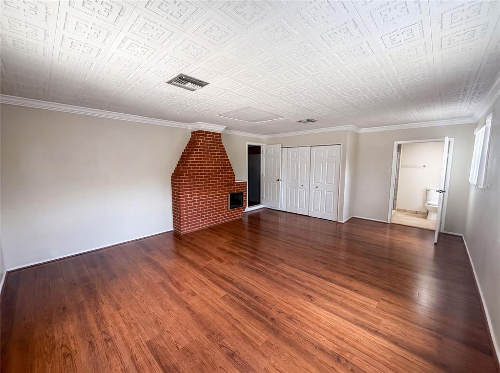 A room with wood-look flooring, a brick fireplace, white paneled ceiling, and an attached bathroom — 345 ACROPOLIS DRIVE, DUNEDIN, FL