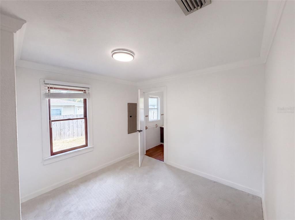 A bedroom with white walls, carpeted flooring, a window, and an open door to a bathroom — 345 ACROPOLIS DRIVE, DUNEDIN, FL