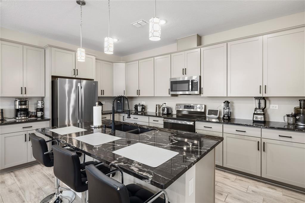 A modern kitchen features light gray cabinets, a black marble island, and stainless steel appliances — 1060 RIVER OTTER WAY, DELAND, FL