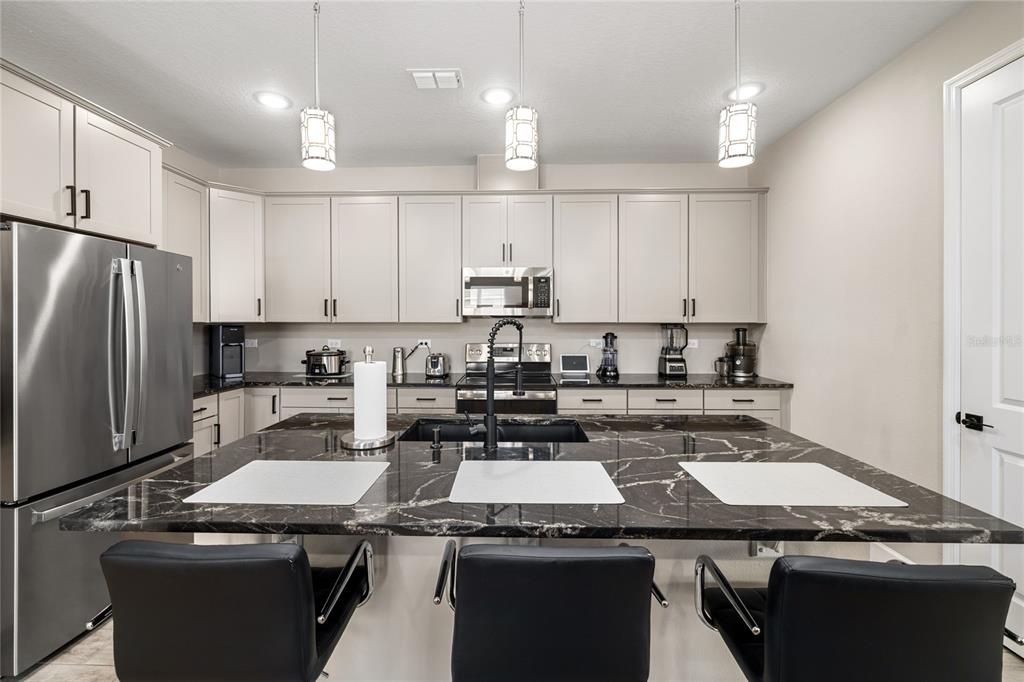A kitchen features light-colored cabinets, stainless steel appliances, and a large black marble island — 1060 RIVER OTTER WAY, DELAND, FL