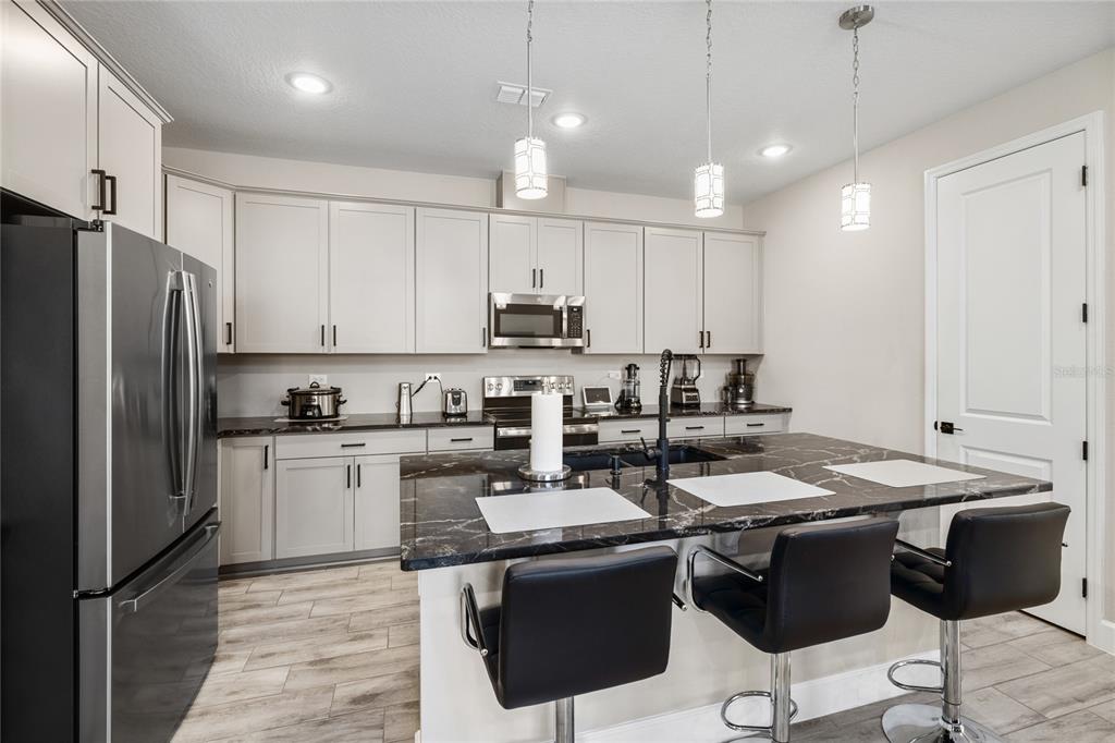 A kitchen features light gray cabinets, a black marble island, and three black bar stools — 1060 RIVER OTTER WAY, DELAND, FL
