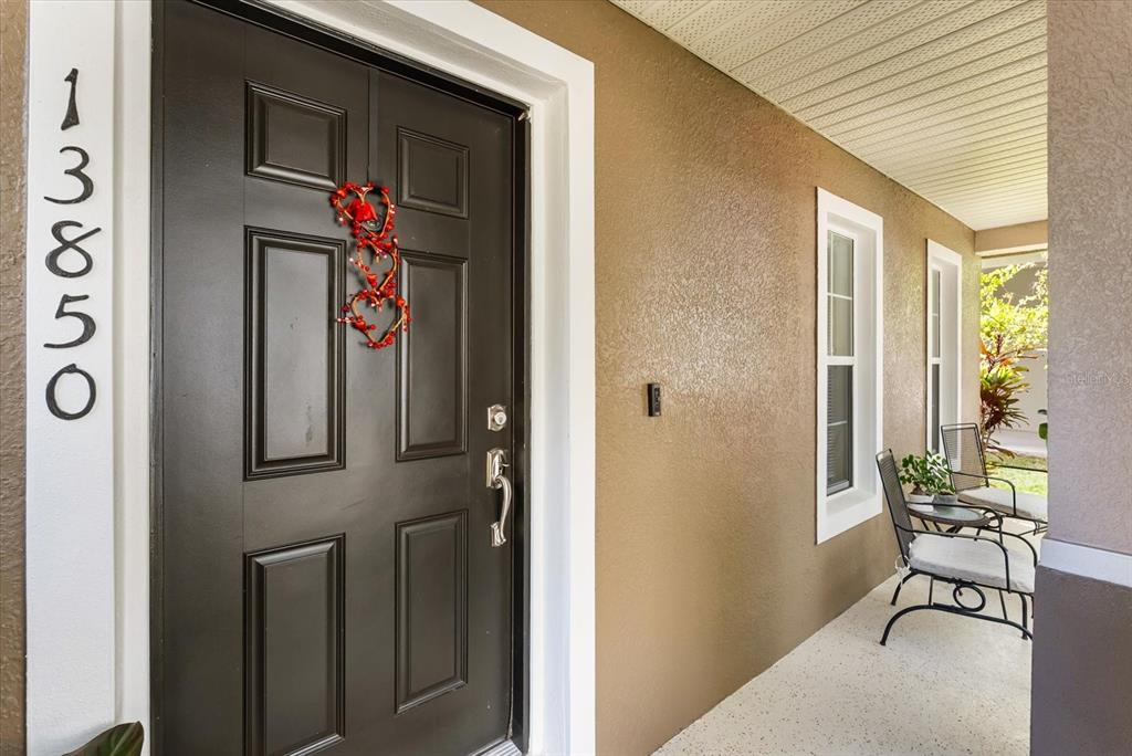 A dark front door with a heart-shaped wreath sits beside a covered porch with chairs — 13850 CAROLINA LAUREL DRIVE, ORLANDO, FL