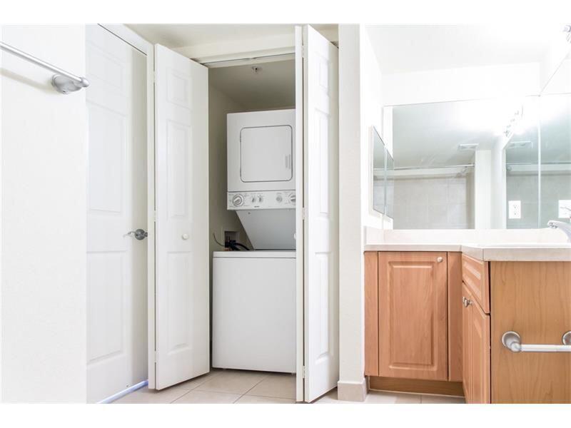 A bathroom features a stacked washer and dryer unit, wooden cabinets, and a large mirror — 6760 Heritage # 6103, Boynton Beach FL 33437, BOYNTON BEACH, FL