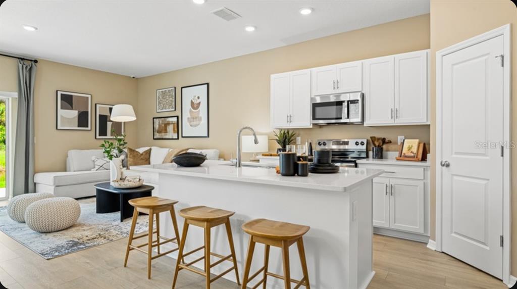 An open-concept kitchen with a white island and stools overlooks a living area — 7211 GRAND FOREST WAY, NOKOMIS, FL