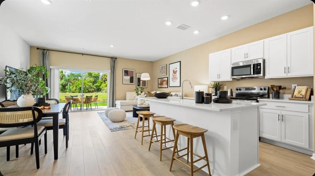 An open-concept kitchen and living area with white cabinets, a breakfast bar, and sliding doors — 7211 GRAND FOREST WAY, NOKOMIS, FL