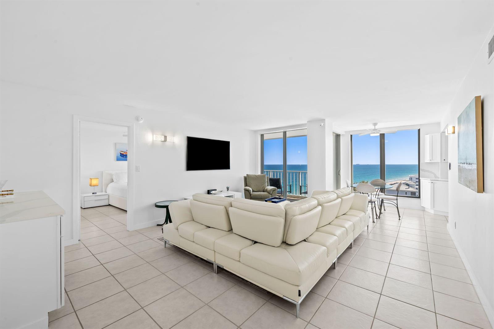 A bright living room features a white sectional sofa, tile flooring, and ocean views — 1010 S Ocean Boulevard # 1502, Pompano Beach FL 33062, POMPANO BEACH, FL