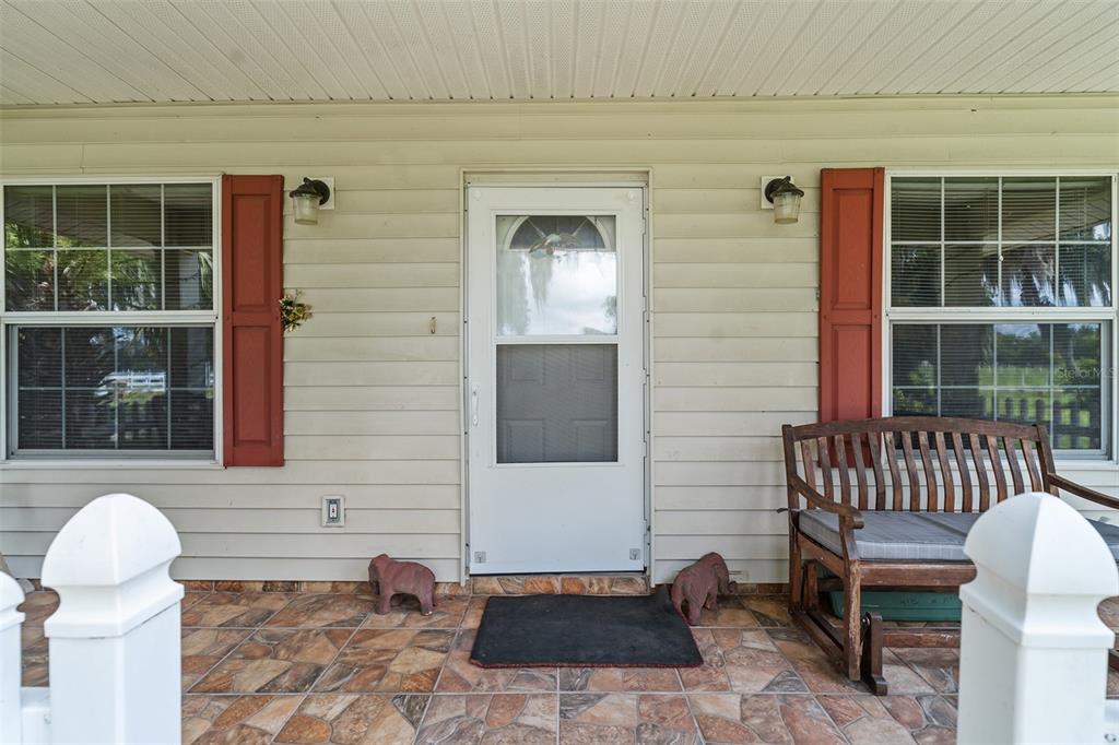 A covered front porch features a white storm door, red shutters, and a wooden bench — 2830 HORTON RD, KISSIMMEE, FL