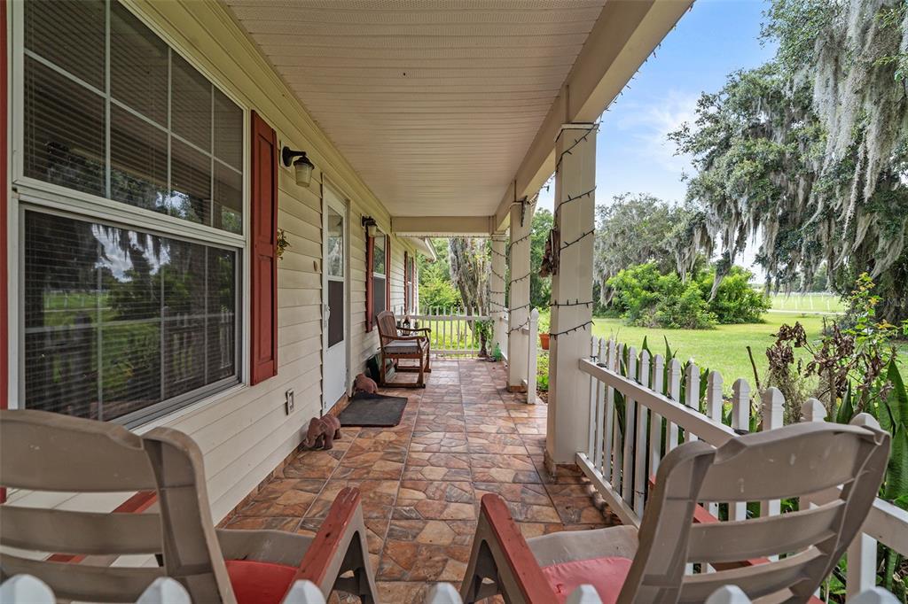 A covered front porch features tiled flooring, white railings, and rocking chairs overlooking a grassy yard — 2830 HORTON RD, KISSIMMEE, FL