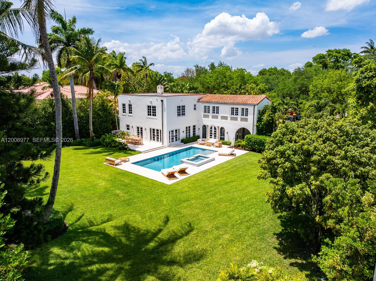 A white stucco house with a tiled roof and arched windows features a covered entryway — 1228 Alhambra Cir, Coral Gables FL 33134, CORAL GABLES, FL