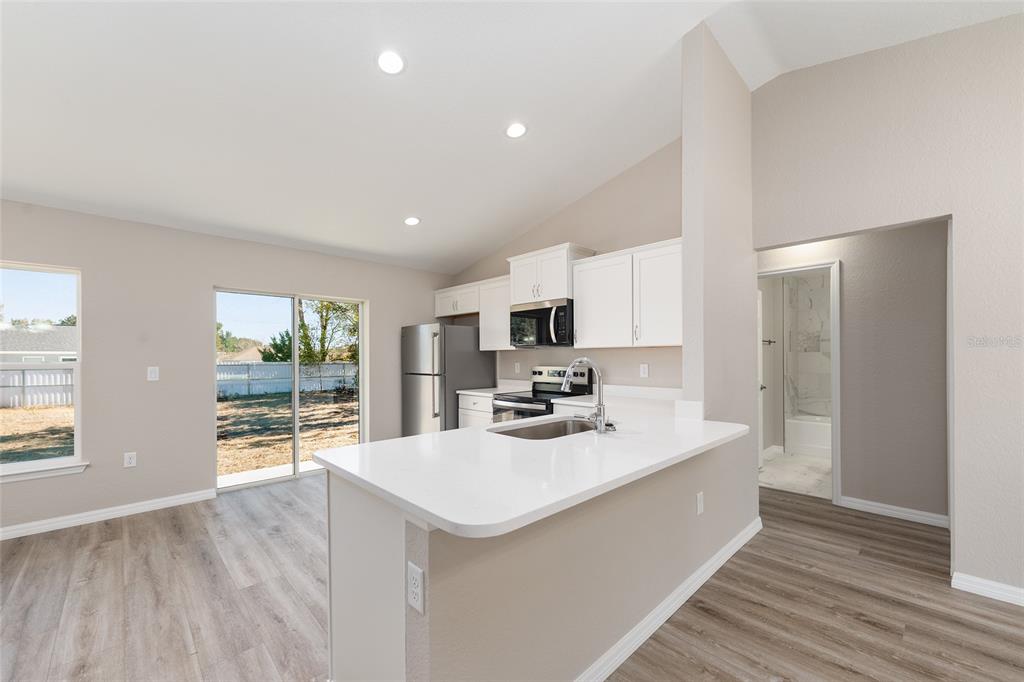A kitchen with white cabinets, stainless steel appliances, and a peninsula overlooking a living area — 14260 SE 34TH COURT, SUMMERFIELD, FL