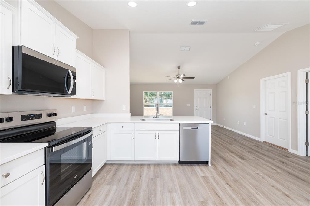 A modern kitchen features white cabinets, stainless steel appliances, and light wood-look flooring — 14260 SE 34TH COURT, SUMMERFIELD, FL